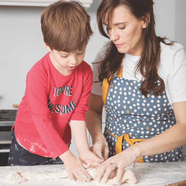 Mother and son rolling dough on marble countertop